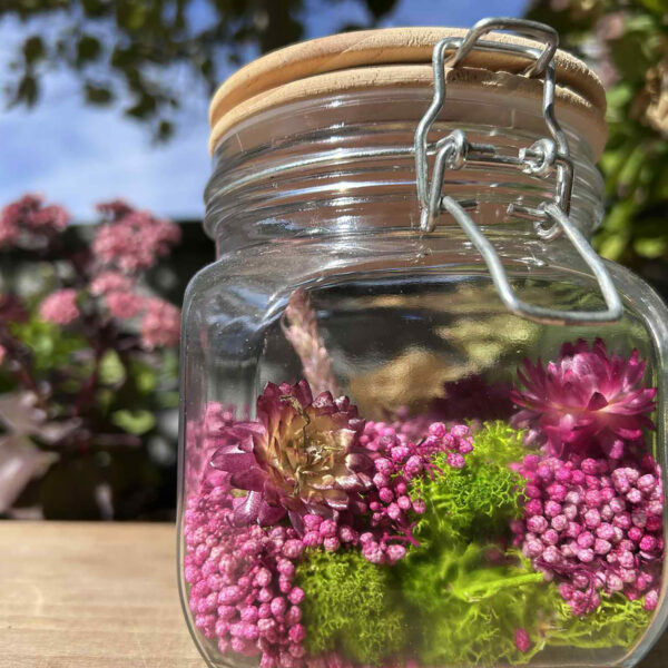 Glazen pot met mos en roze bloemen